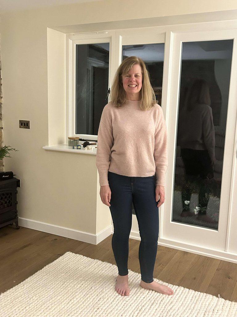 A full length photo of our client Rachel smiling in her home after she was able to lose weight with a bad back.